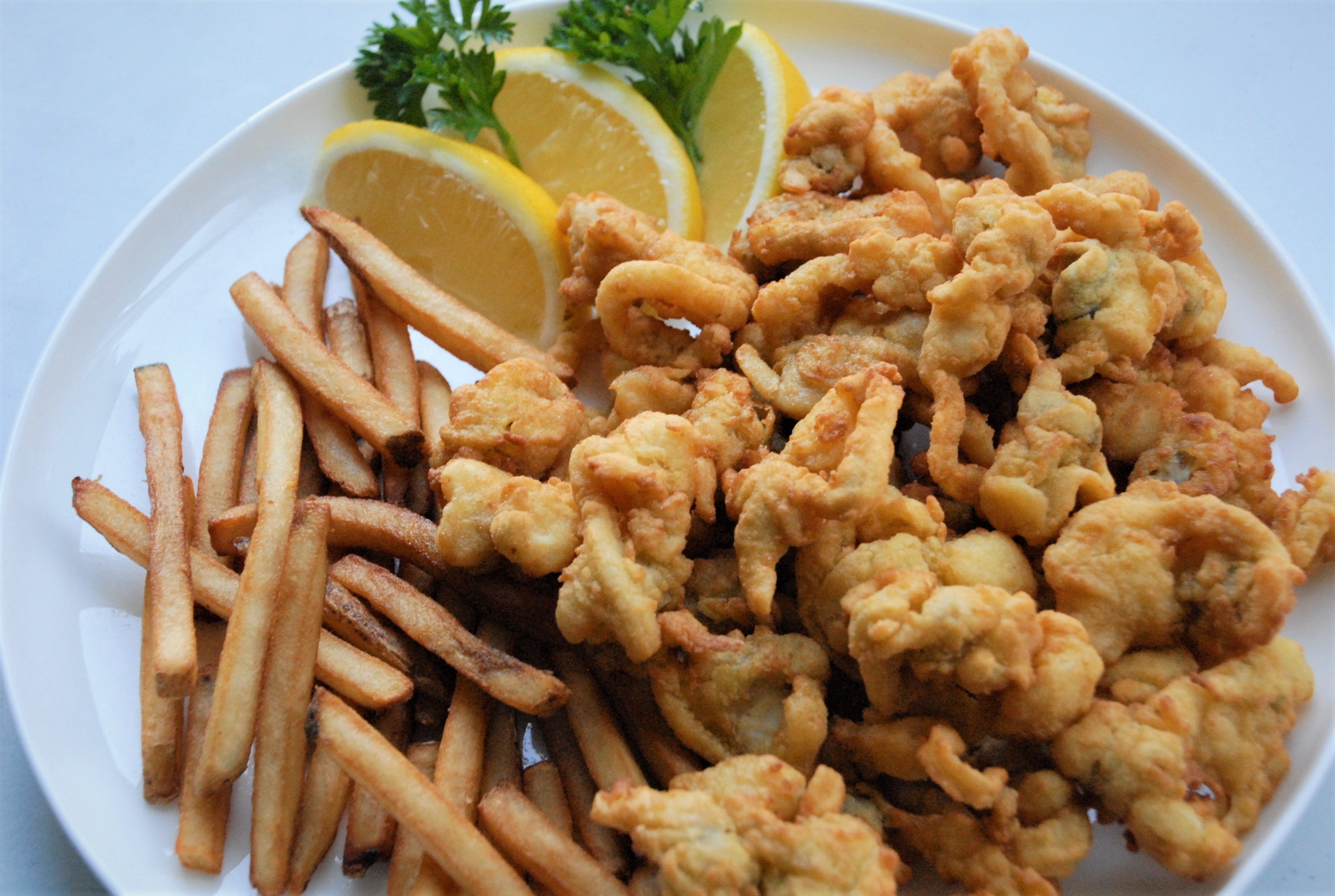 Fried calamari with French fries and lemon wedges on a white plate.